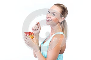 Beautiful young woman eating cereals and fruits over white background.