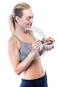 Beautiful young woman eating cereals and fruits over white background.