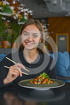 Beautiful young woman eating chinese food called Wok with chopsticks. Wok with meat and fried asparagus in a plate