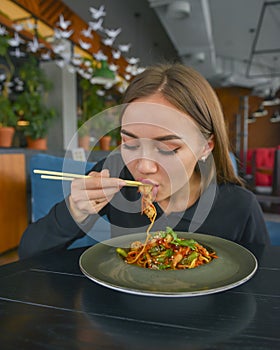 Beautiful young woman eating chinese food called Wok with chopsticks. Wok with meat and fried asparagus in a plate