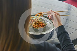 Beautiful young woman eating chinese food called Wok with chopsticks. Wok with meat and fried asparagus in a plate