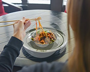 Beautiful young woman eating chinese food called Wok with chopsticks. Wok with meat and fried asparagus in a plate