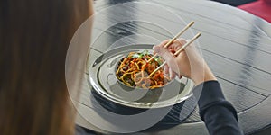 Beautiful young woman eating chinese food called Wok with chopsticks. Wok with meat and fried asparagus in a plate