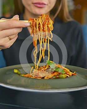 Beautiful young woman eating chinese food called Wok with chopsticks. Wok with meat and fried asparagus in a plate