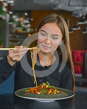 Beautiful young woman eating chinese food called Wok with chopsticks. Wok with meat and fried asparagus in a plate