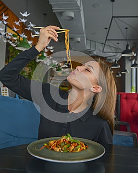 Beautiful young woman eating chinese food called Wok with chopsticks. Wok with meat and fried asparagus in a plate