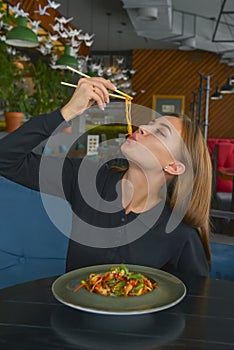 Beautiful young woman eating chinese food called Wok with chopsticks. Wok with meat and fried asparagus in a plate