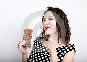 Beautiful young woman eating a chocolate bar, wears a dress with polka dots. expresses different emotions