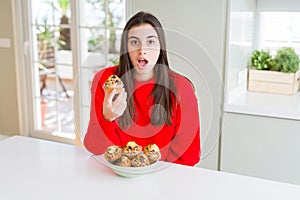 Beautiful young woman eating chocolate chips muffins scared in shock with a surprise face, afraid and excited with fear expression