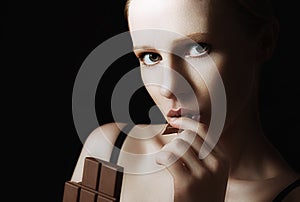 beautiful young woman eating chocolate on a dark