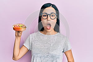 Beautiful young woman eating hotdog scared and amazed with open mouth for surprise, disbelief face