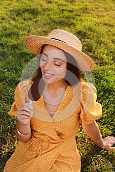 Beautiful young woman eating ice cream glazed in chocolate on green grass outdoors