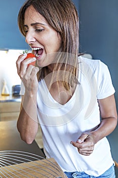 Beautiful young woman eating a tomato in a modern kitchen