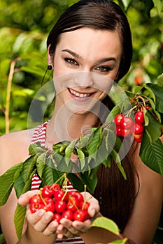 Beautiful young woman eats cherry on plantation