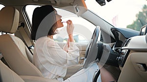 Beautiful young woman in elegant business clothing applying makeup in the car using the mirror to apply red lip gloss as