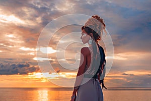 Beautiful young woman in elegant dress on the beach at sunset