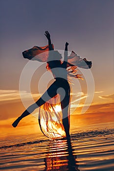 beautiful young woman in elegant dress dancing on water at sunset