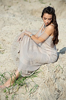 Beautiful young woman in elegant dress sitting on the beach at sunset