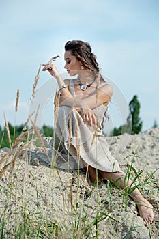 Beautiful young woman in elegant dress sitting on the beach at sunset