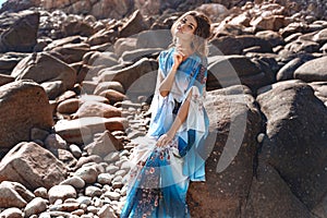 Beautiful young woman in elegant stylish dress  on stone beach at sunset