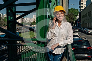Beautiful young woman engineer or supervisor, wearing a safety helmet, talking on a cell phone while taking a short break