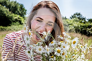 Beautiful young woman enjoying eating camomile field flowers for fun