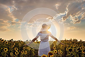 Beautiful young woman enjoying nature on the field of sunflowers at sunset