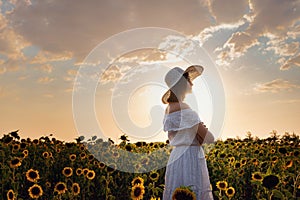 Beautiful young woman enjoying nature on the field of sunflowers at sunset