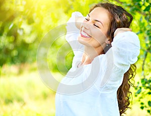 Beautiful young woman enjoying nature outdoor. Happy smiling brunette girl relaxing in the summer park