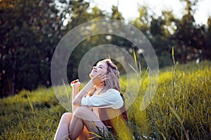 Beautiful young woman enjoying a picnic in nature. Girl sitting on grass, rest, relaxation