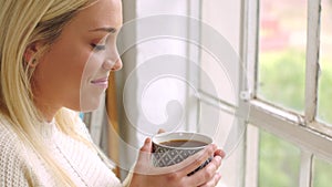 A beautiful young woman enjoying a warm cup of coffee and smiling in the morning. One happy blonde female drinking tea