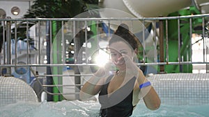 Beautiful young woman enjoys spending time in the water park smiling showing hands sign heart shape looking at camera