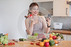 Beautiful young woman in exercise clothes having fun in a cute kitchen at home. Using the phone to study information And