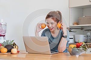 Beautiful young woman in exercise clothes having fun in a cute kitchen at home. Using your laptop to prepare vegan fruit