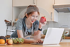 Beautiful young woman in exercise clothes having fun in a cute kitchen at home. Using your laptop to prepare vegan fruit