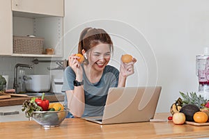 Beautiful young woman in exercise clothes having fun in a cute kitchen at home. Using your laptop to prepare vegan fruit