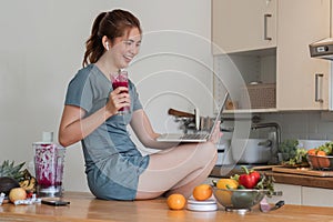 Beautiful young woman in exercise clothes having fun in a cute kitchen at home. Using your laptop to prepare vegan fruit