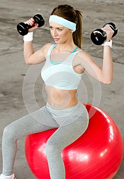 Beautiful young woman exercising with dumbbells and fitness ball