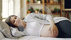 Beautiful young woman expecting mother is lying on bed at home and stroking her belly expressing love for her baby. Nice