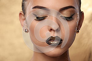 Beautiful young woman with extravagant makeup on golden background, closeup