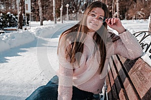 Beautiful young woman in eye glasses knitted sweater in winter park. Cold weather outdoors. Snow Happy smiling portrait
