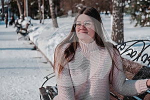 Beautiful young woman in eye glasses knitted sweater in winter park. Cold weather outdoors. Snow Happy smiling portrait