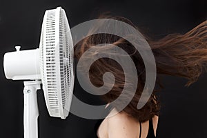 Beautiful young woman face to electric fan enjoying cold wind to refreshing up