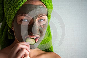 Beautiful young woman with facial mask on her face holding slices of cucumber