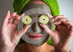 Beautiful young woman with facial mask on her face holding slices of cucumber