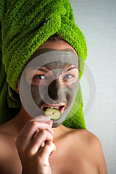 Beautiful young woman with facial mask on her face holding slices of cucumber