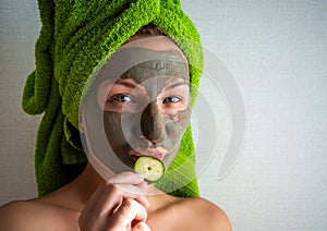 Beautiful young woman with facial mask on her face holding slices of cucumber