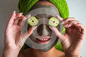 Beautiful young woman with facial mask on her face holding slices of cucumber