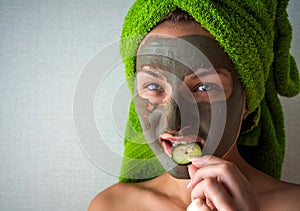 Beautiful young woman with facial mask on her face holding slices of cucumber