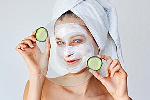 Beautiful young woman with facial mask on her face holding slices of cucumber. Skin care and treatment, spa and cosmetology